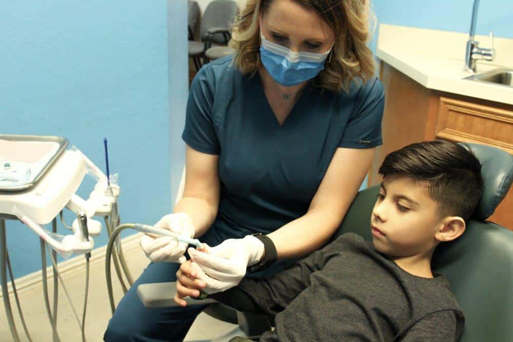 Bellmead Kids Dentistry team member gives a hands on demonstration what the teeth cleaning tool feels like to a pediatric patient in the treatment room