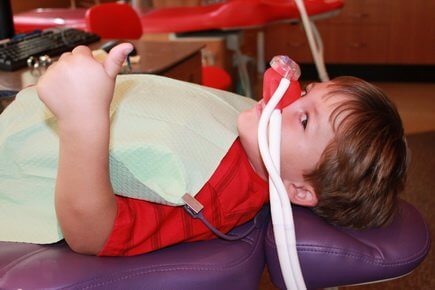 Bellmead Kids Dentistry patient in the treatment room with a sedation mask on his nose showing the thumb up signal